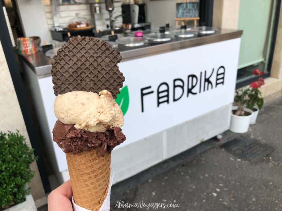 close up of double scoop ice cream cone with Fabrika ice cream cart behind 