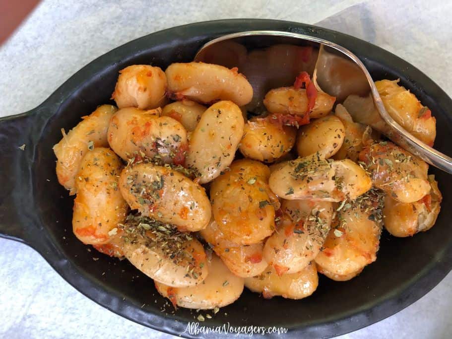 black earthen ware oval dish with baked lima beans and serving spoon