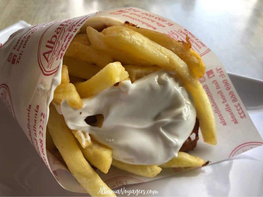 Sufflaque with fries spilling out and big blob of sauce wrapped in paper in Tirana