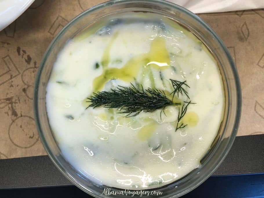 a glass bowl of white yogurt soup garnished with a prig of dill and olive oil, one of the best things to eat in summer in Tirana