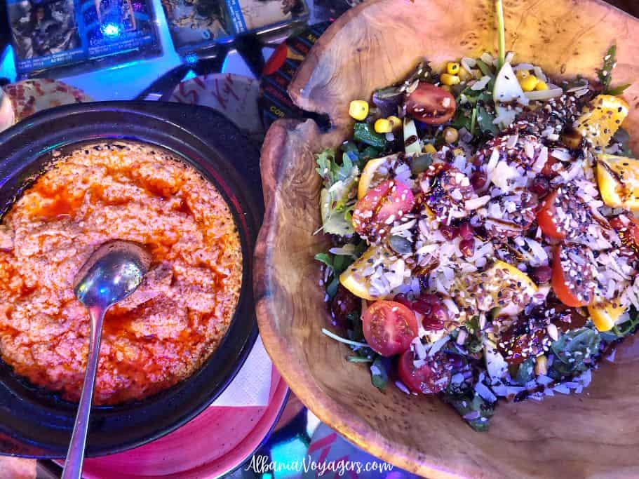 big wooden bowlof mixed salad and round dish of tave dheu with spoon from overhead at Tymi restaurant in Tirana