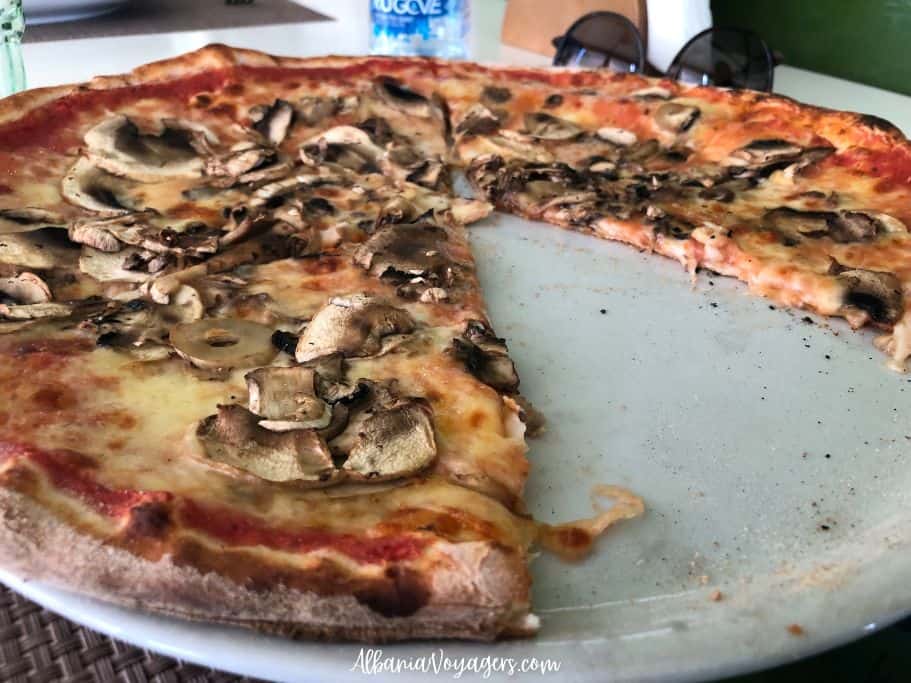 large mushroom pizza with one slice missing on white plate at Saporita in Tirana