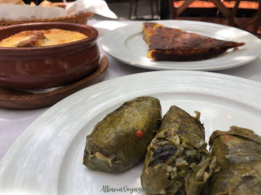 earthenware pot of tave kosi and white plates with leek pie and suffed grape leaves at Oda's Garden in Tirana