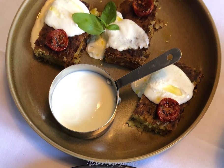 3 pieces of Pispili me Presh with yogurt sauce on brown earthenware plate in Tirana