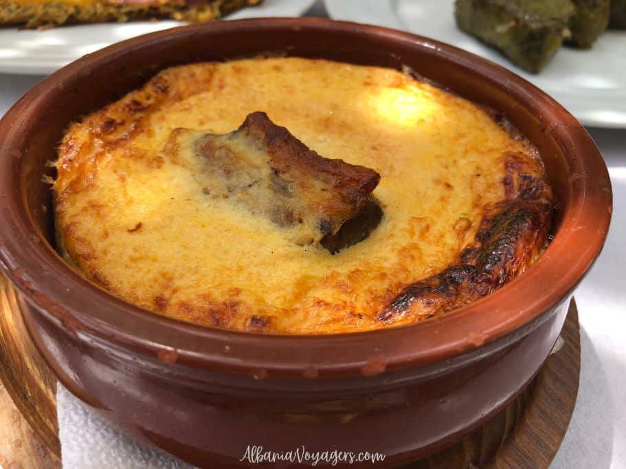 brown earthenware dish with tave kosi and big piece of lamb in the middle