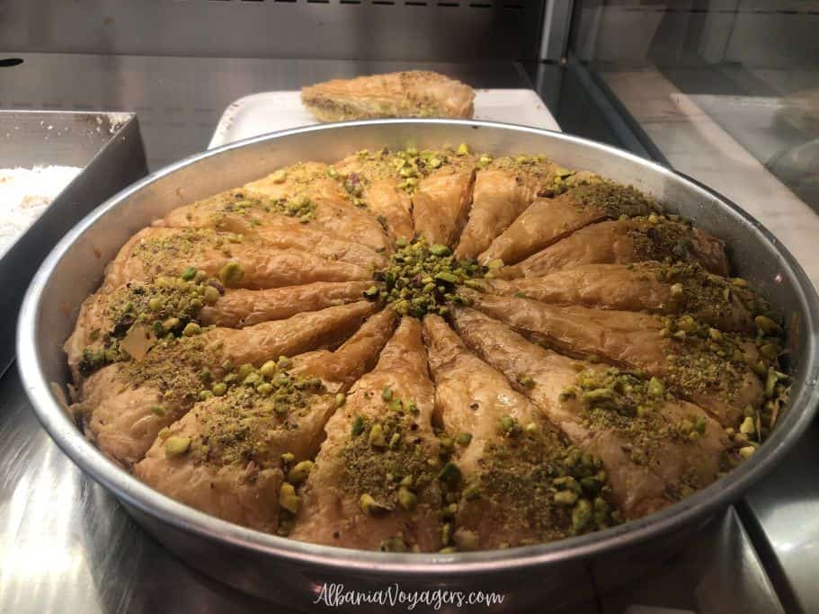 big round metal baking dish of baklava garnished with crushed pistachios, a sweet Albanian food