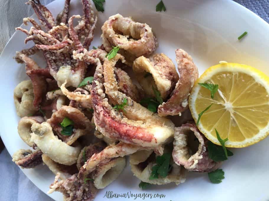 lighlty fried big pieces of kalamari on white palte with half a lemon, in Tirana
