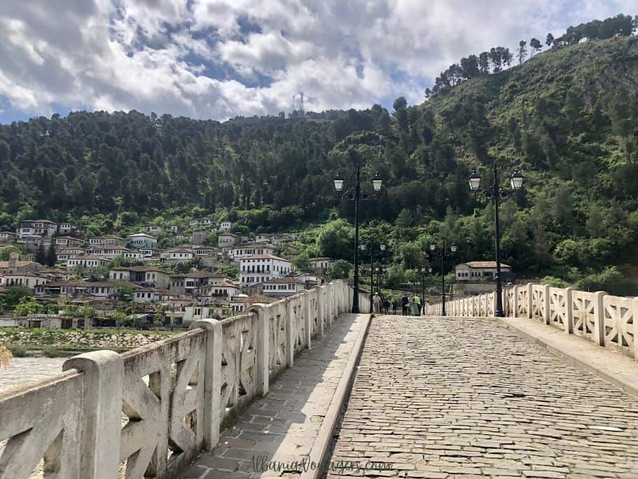 looking over stone arched bridge to old town on other side and green hill in Berat