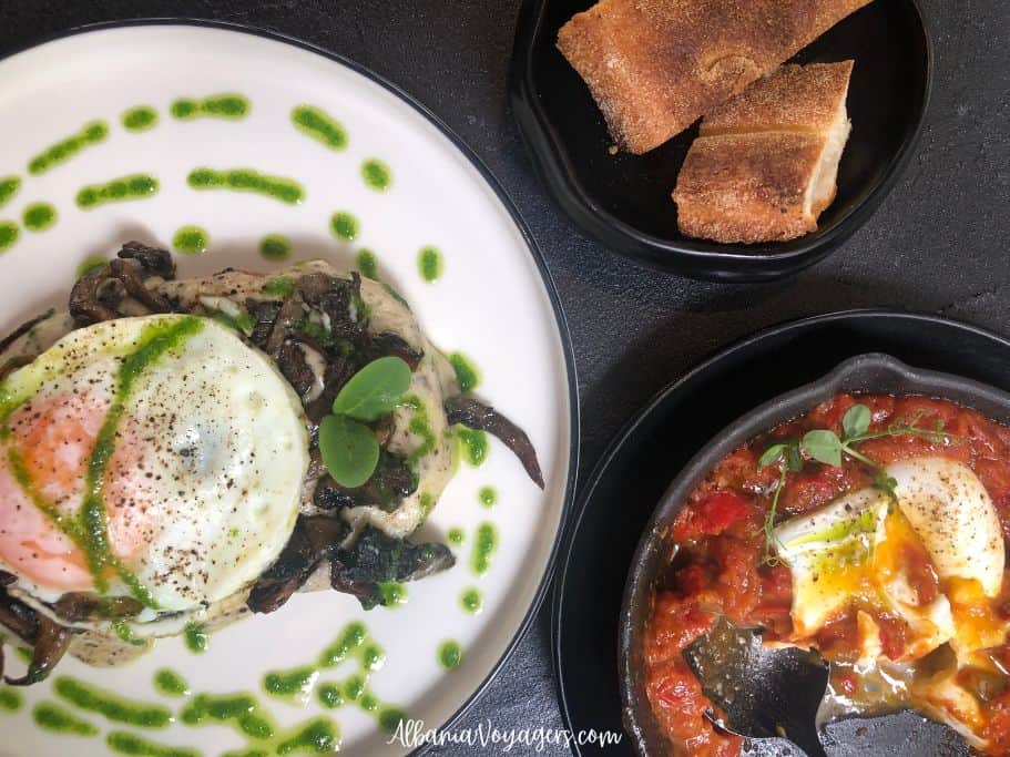 Croque madame on white plate garnished with sprial of green sauce and eggs shashuka in dark casserole dish with baske to bread at Painted Black in Tirana