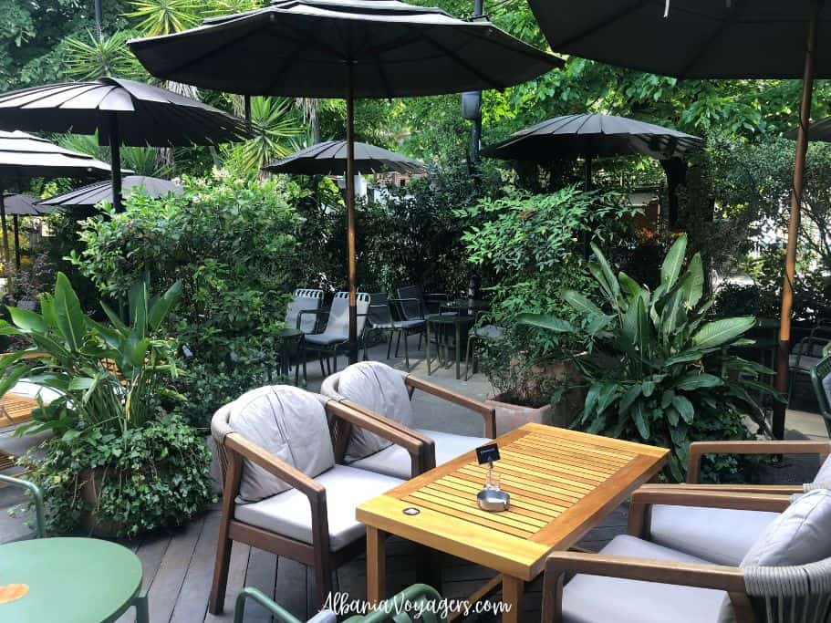 outdoor terrace at Mulliri Gourmet in Tirana with black umbrellas, lots of greenery and wooden tables