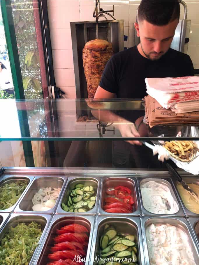 young man assembling a sufflaq behind a super clean counter with condiments at 1Maji in Durres
