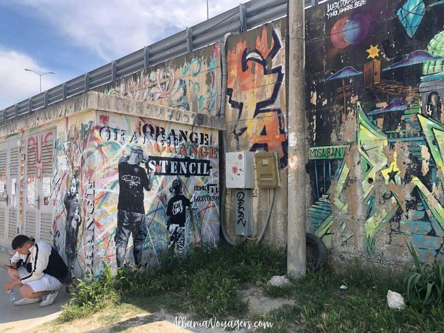 cement wall full of graffiti and young man crouching down in Golem