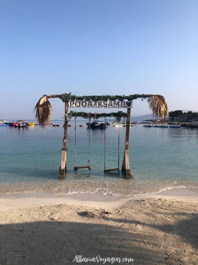 two swings in the sea with Poda Ksamil sign at Poda Beach