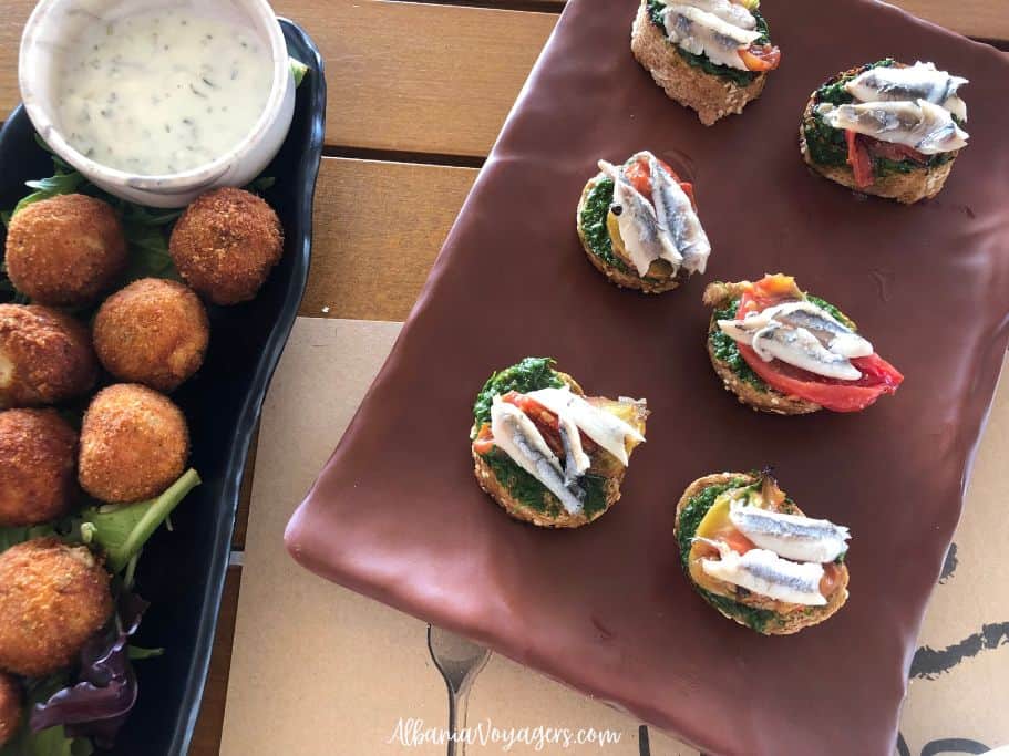 brown plate of burchetta with anchovies and black plate with fish balls and dill sauce at Himara 28 in Himare
