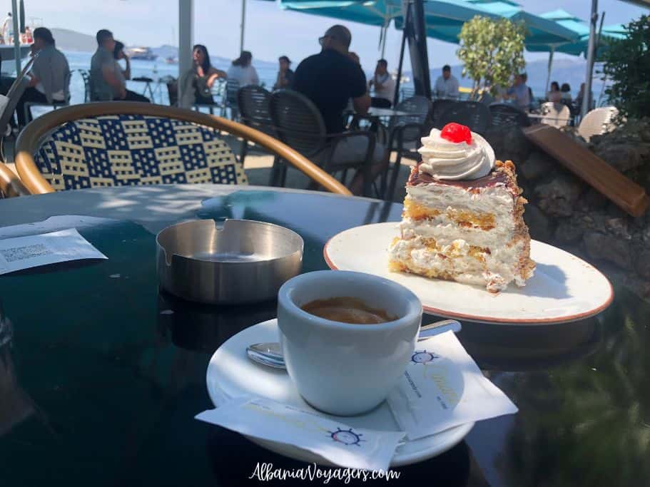 cup of coffee and piece of cake on dark table with sea in the background at Limani in Saranda