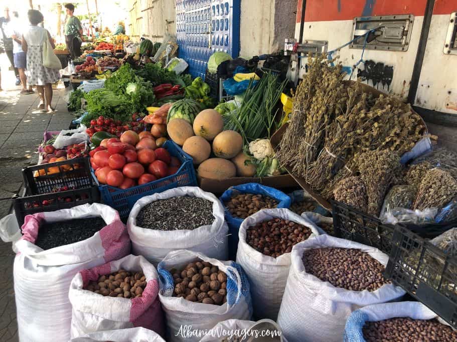 white burlap bags of walnuts and beans with stack os dried mountian flower tea and bins of fresh fruit in Saranda market 