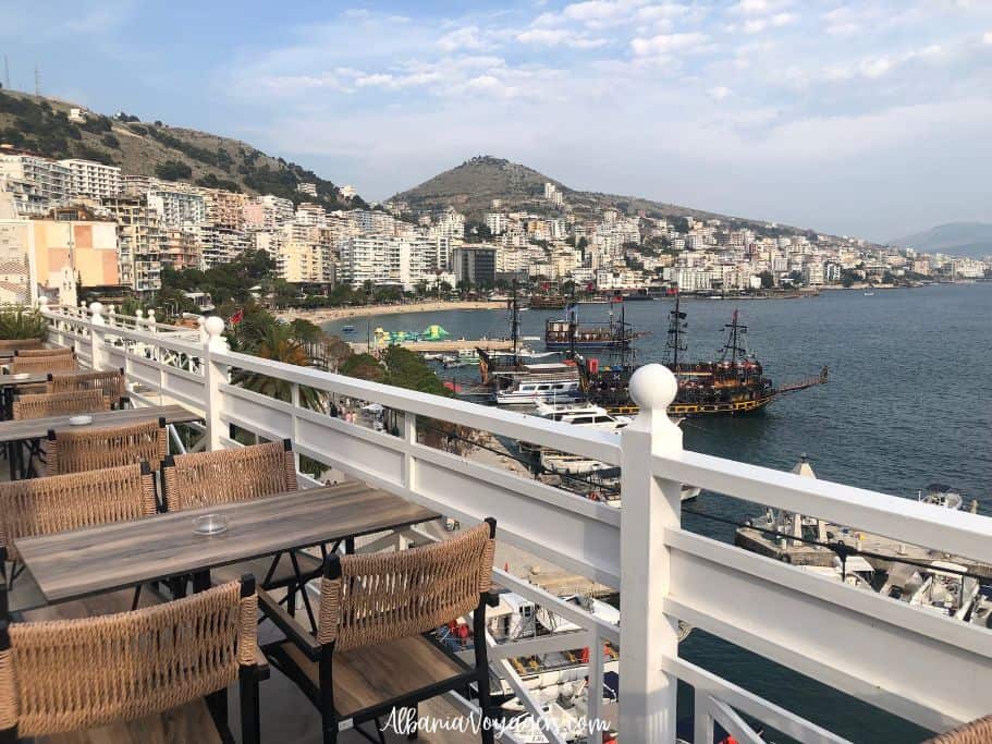 overlooking Saranda from rooftop terrace with white railing and brown tables and chairs