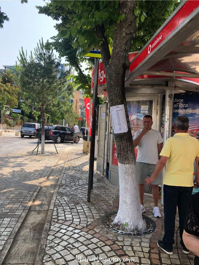 two men standing and smoking in front of bus stop in Saranda