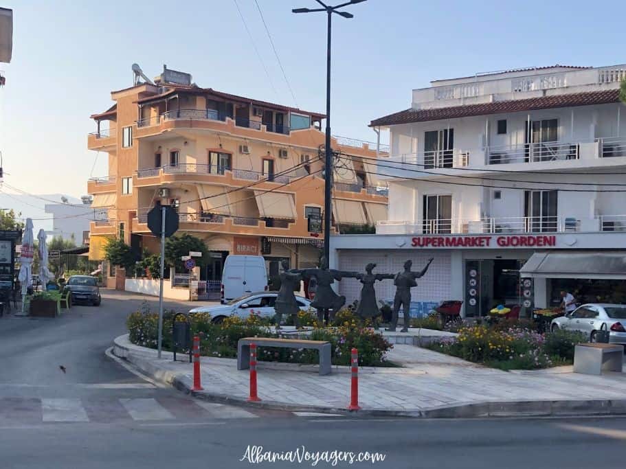 supermarket and low rise building with statue of 4 Albanian dancers in Ksamil