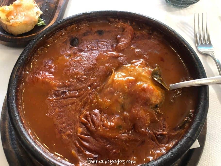 earthenware dish of tave krapi with spoon on white table cloth, a traditional food of Shkoder in northern Albania