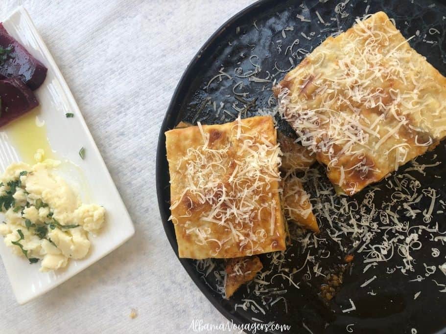 two pieces of moussaka on a black plate with white side plate of beets and potato in Himare.