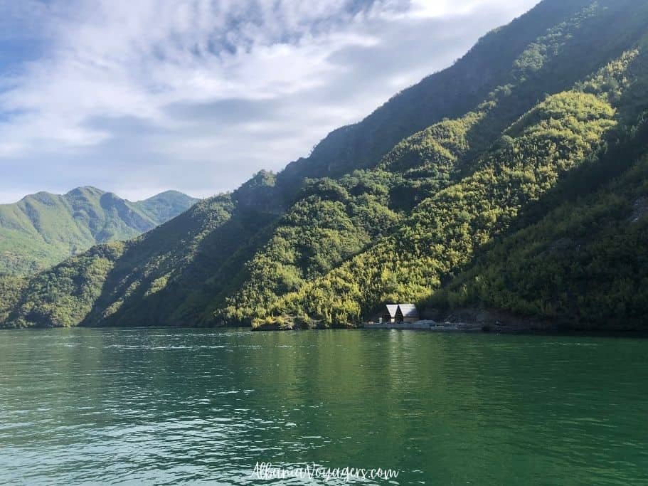 Komani Lake with forrested mountains and small lodges on shore, one of the best things to do in Albania