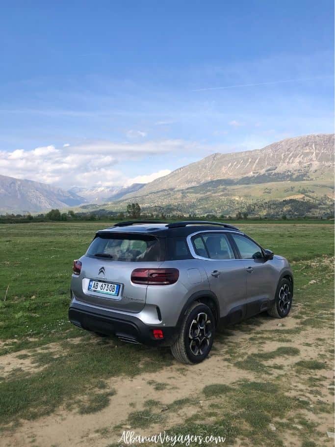 grey SUV parked on grass with mountains in background
