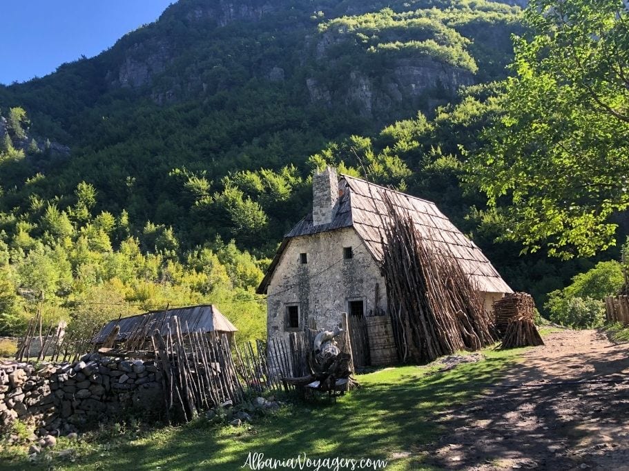 stone farm house with tall stick leaning up against it and mountains behind in Theth