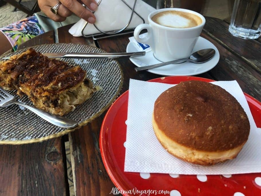 red and white polka dot plate with donut, black and white plate with piece of patsavoura and white cup of coffee on wooden table at Kanelle in Shkoder