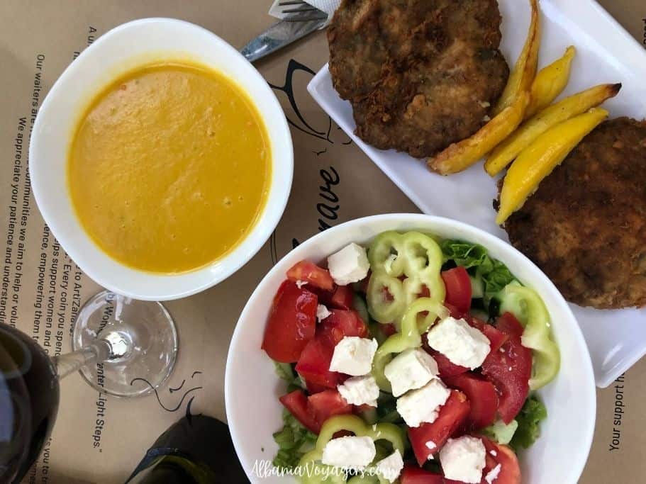 white bowl of creamy soup, bowl of Greek salad and white plate of two hamburger patties and potatoes at Arti-Zanave, a great place to eat in Shkoder