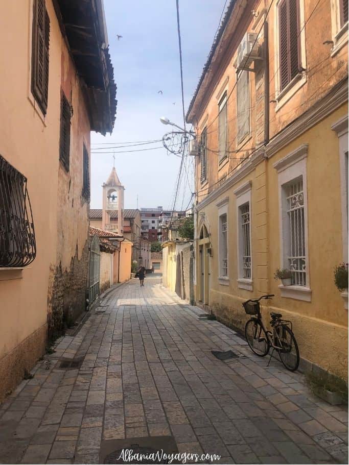 quiet lane with  yellow painted buildings and church steeple in Shkoder Old Town