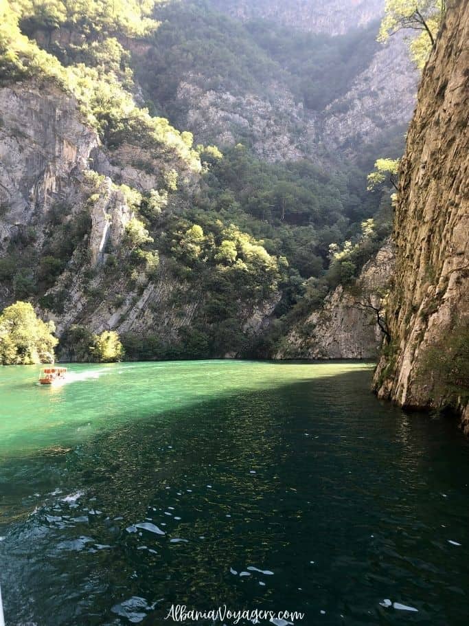 green water and high fjords on both sides with small boat on the Shala River