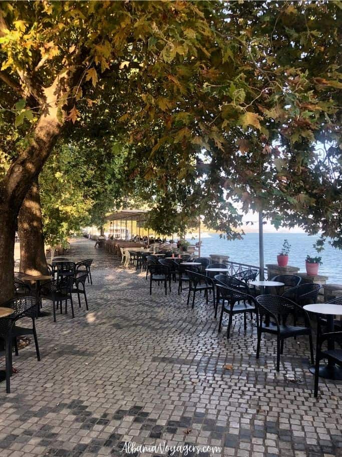 main road in Shiroka with cafe tables and the lake
