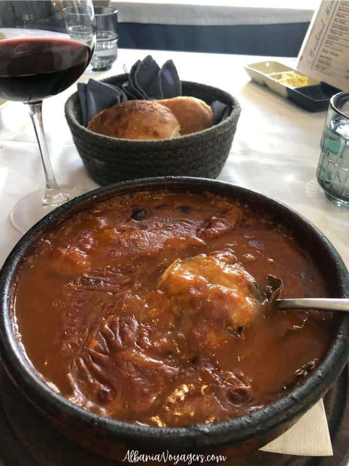 earthenware dish with tomato sauce and big pieces of fish with wine glass and basket of bread at Marina Seafood Restaurant in Shkoder