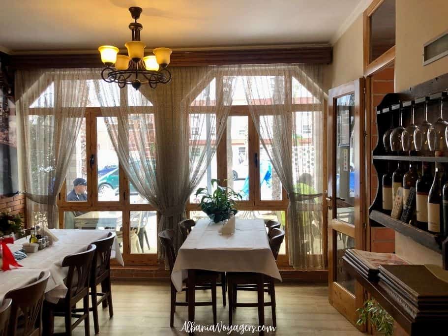 dining room with big windows and wood tables and chairs set in white linen table cloths at Restorant 4 Stinet near Vlore Old Town