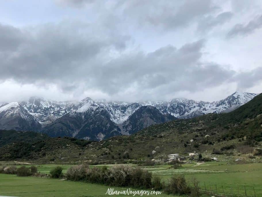snowcapped mountains with green fields in front on drive to Vlore from Saranda