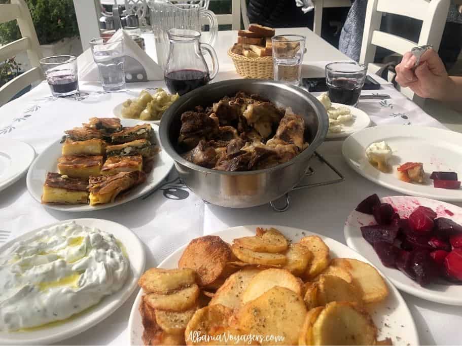 table full of plates of food and big metal bowl of grilled lamb and wine glasses at Tamo's Farm near Saranda