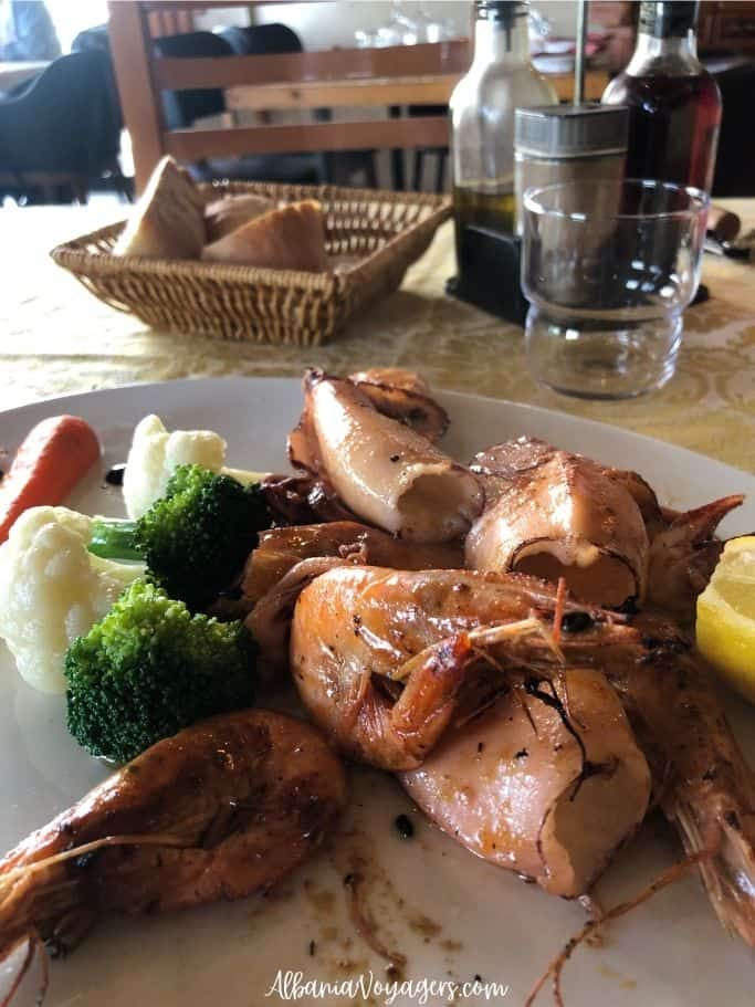 white plate of grilled kalamari and shrimp with basket of bread at Kantina Balaj