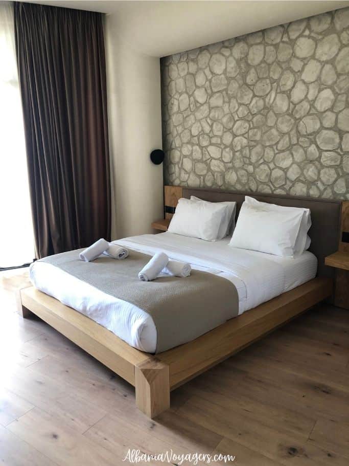 large bed with stone accent wall and bleached wood floors at Brooklyn Hotel Vlore
