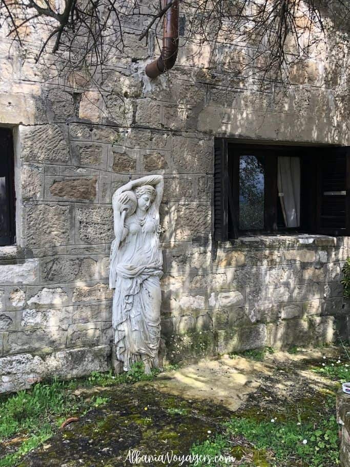 stone statue of maiden holding jug beside stone wall