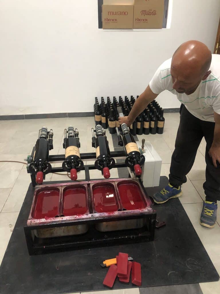 man leaning over 4 wine bottles being dipped in red wax at Nurellari Winery
