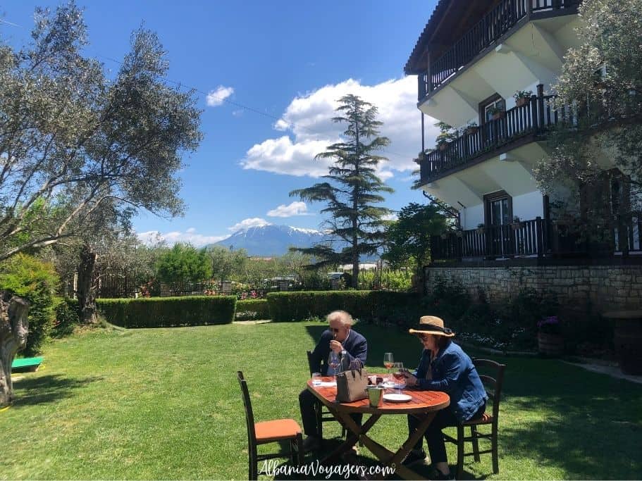 outdoor wine garden with couple at table and views of snow capped Mt Tomorri in background