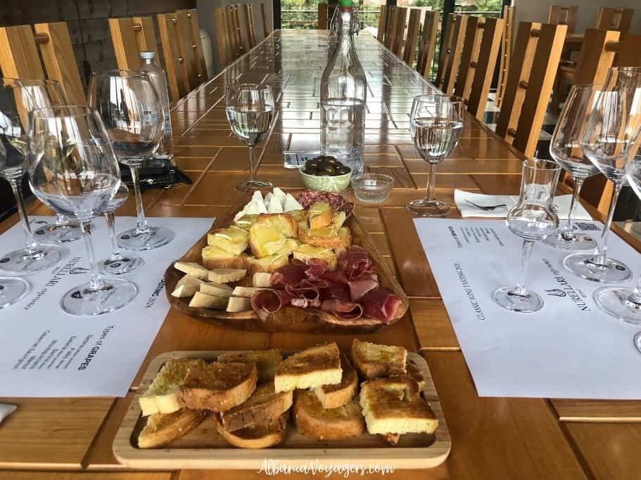 long wooden table with platters of cheese, meats, bread and olives and set with wine glasses for tastings at Nurellari Winery near Berat