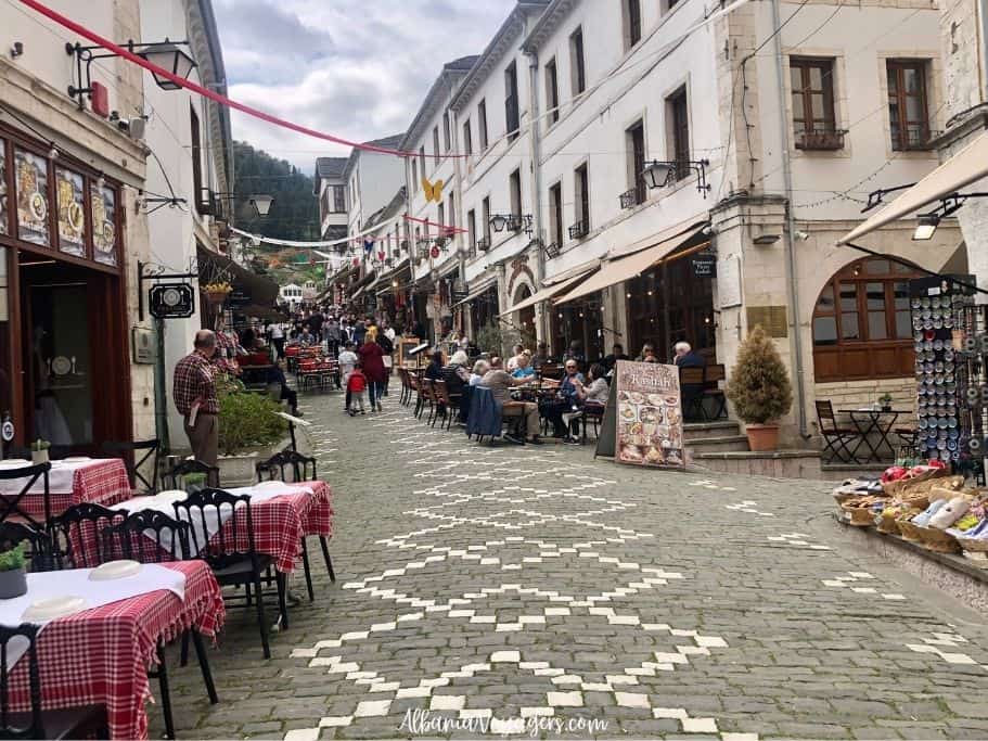 Ottoman bazaar in Gjirokaster with patterned cobblestone street and restaurant tables with red checked table cloths