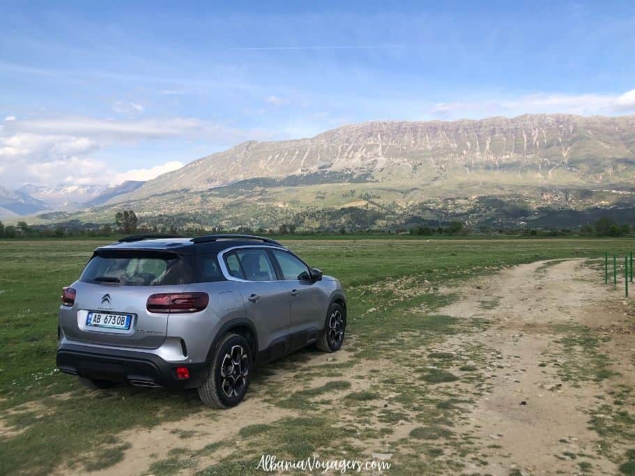 grey SUV parked on grass with mountains in background